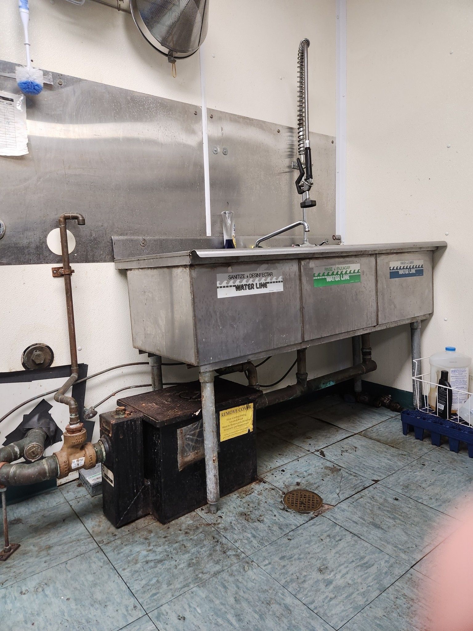 A stainless steel commercial sink with three basins is in a dirty kitchen.