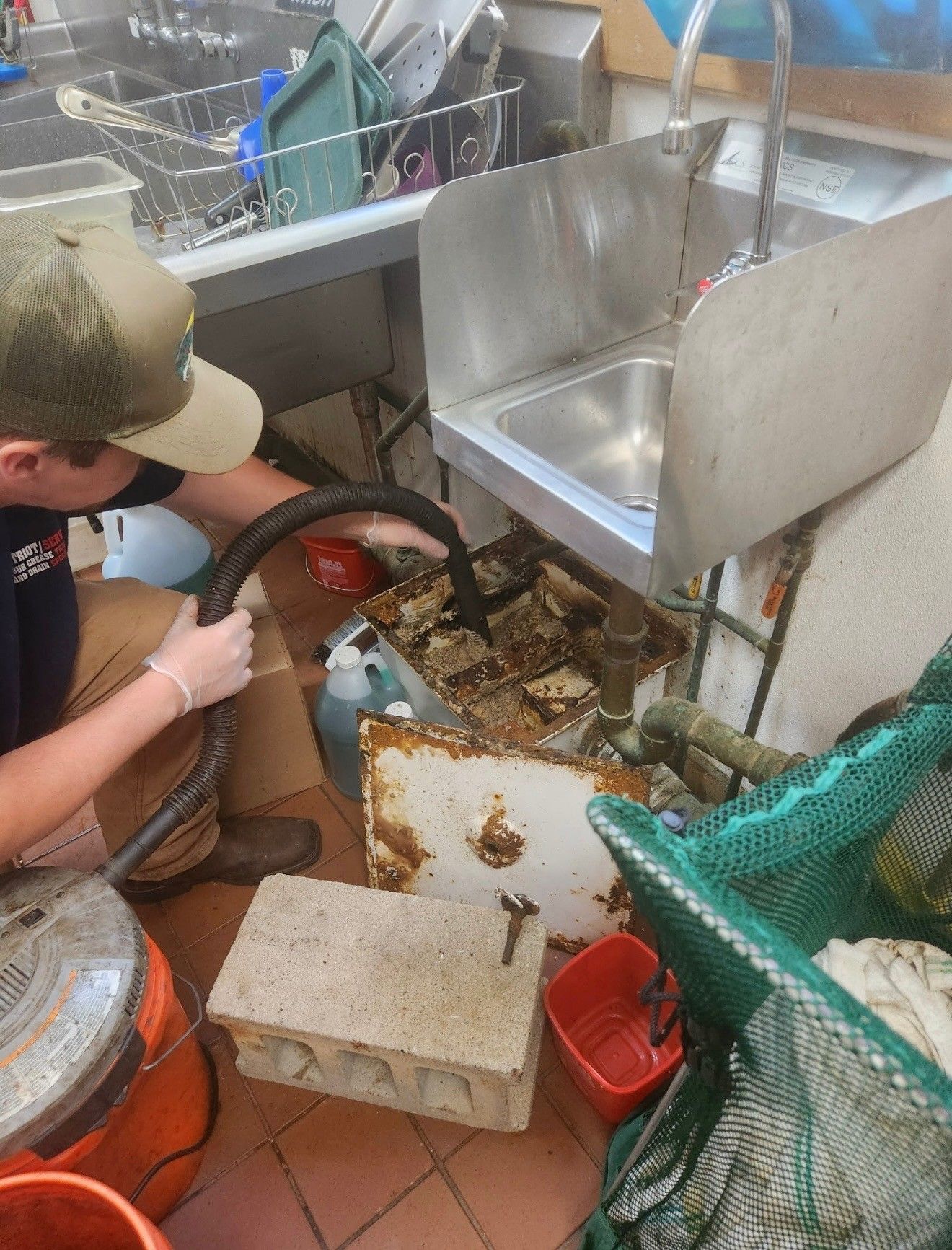 Person wearing gloves cleaning up a cluttered kitchen area with a hose and cleaning materials.