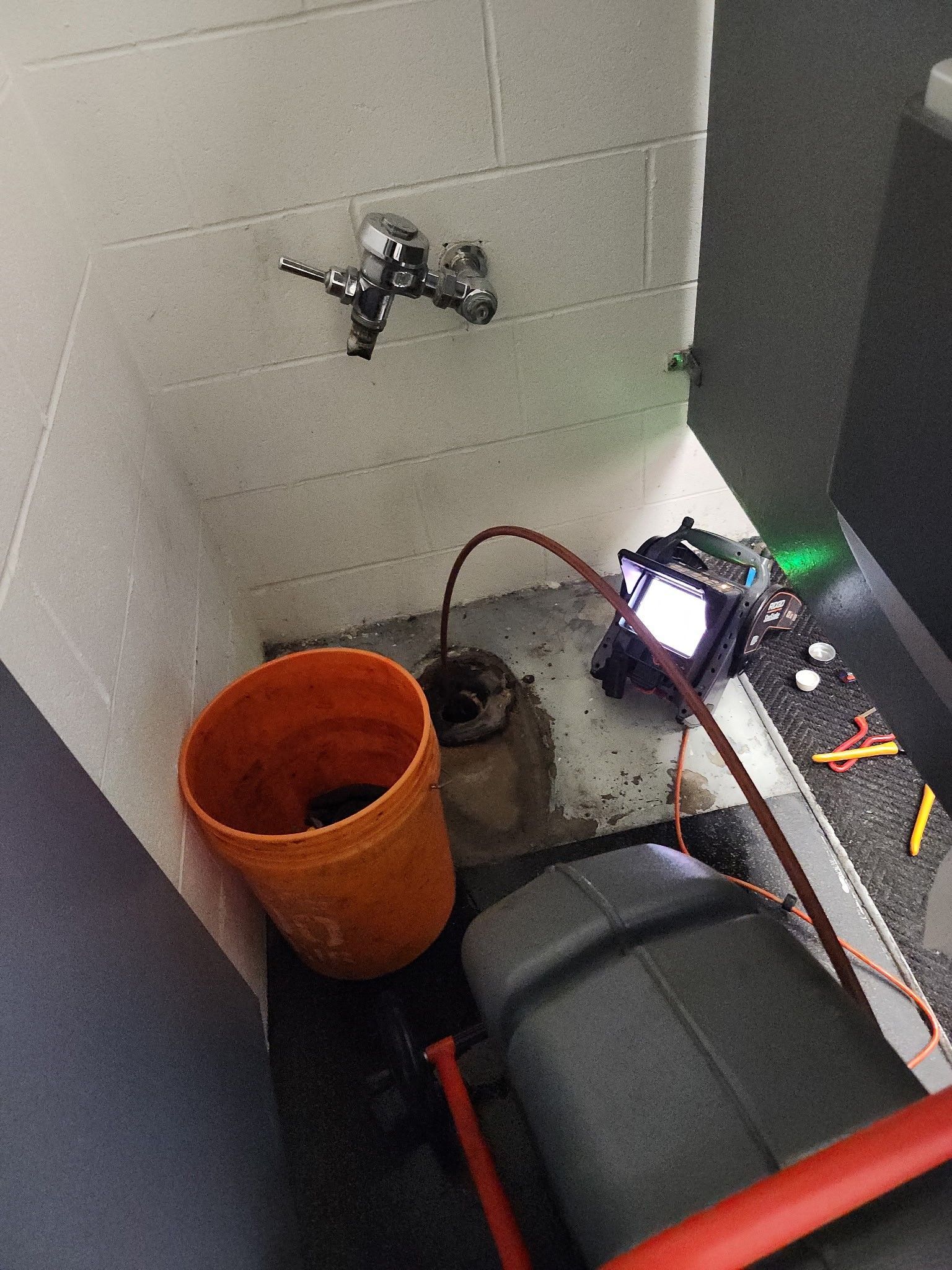 A plumbing repair: orange bucket near drain. Tools and equipment on dark floor by sink.