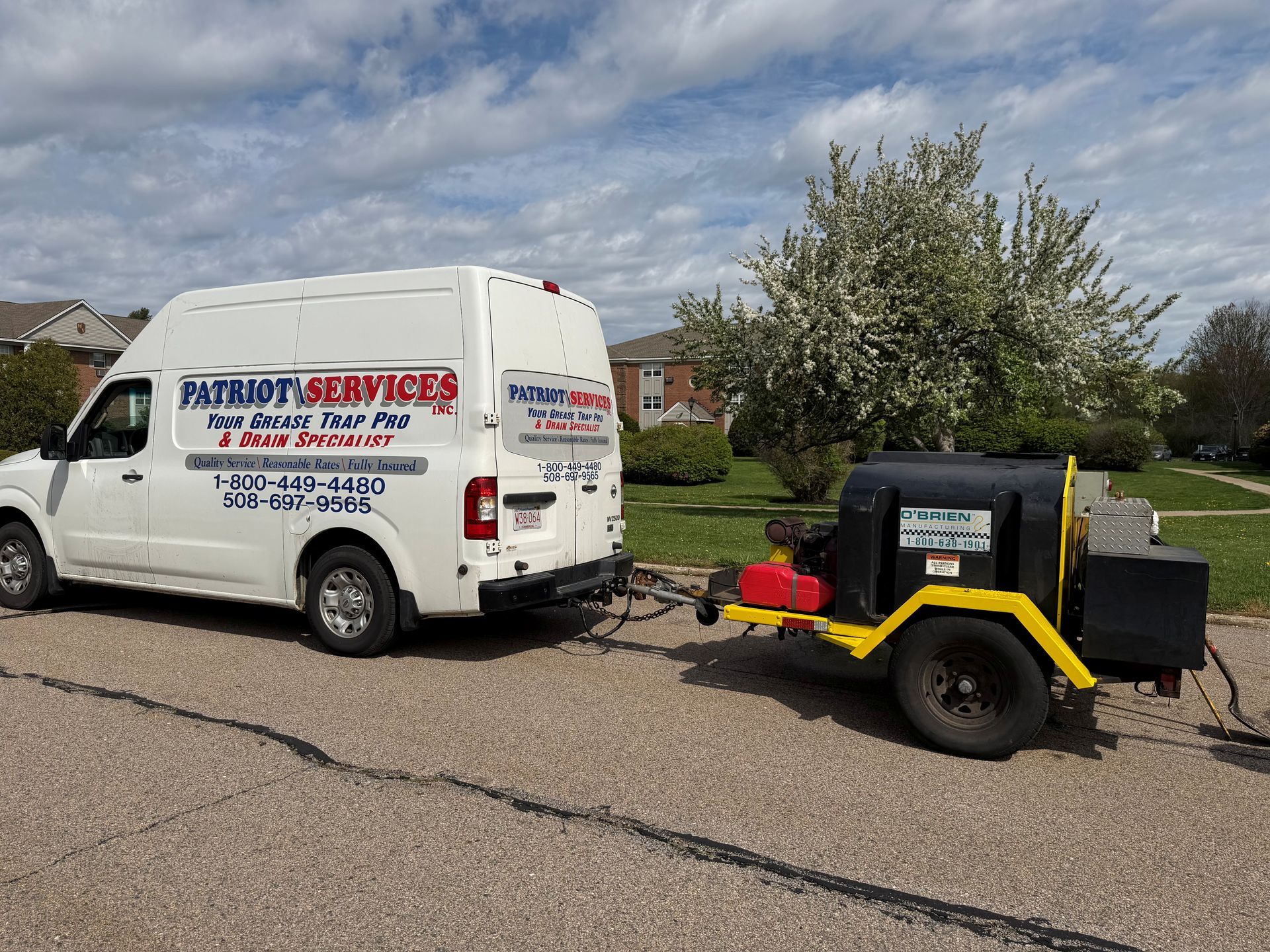 White service van towing a small black utility trailer on a roadside under a cloudy sky.