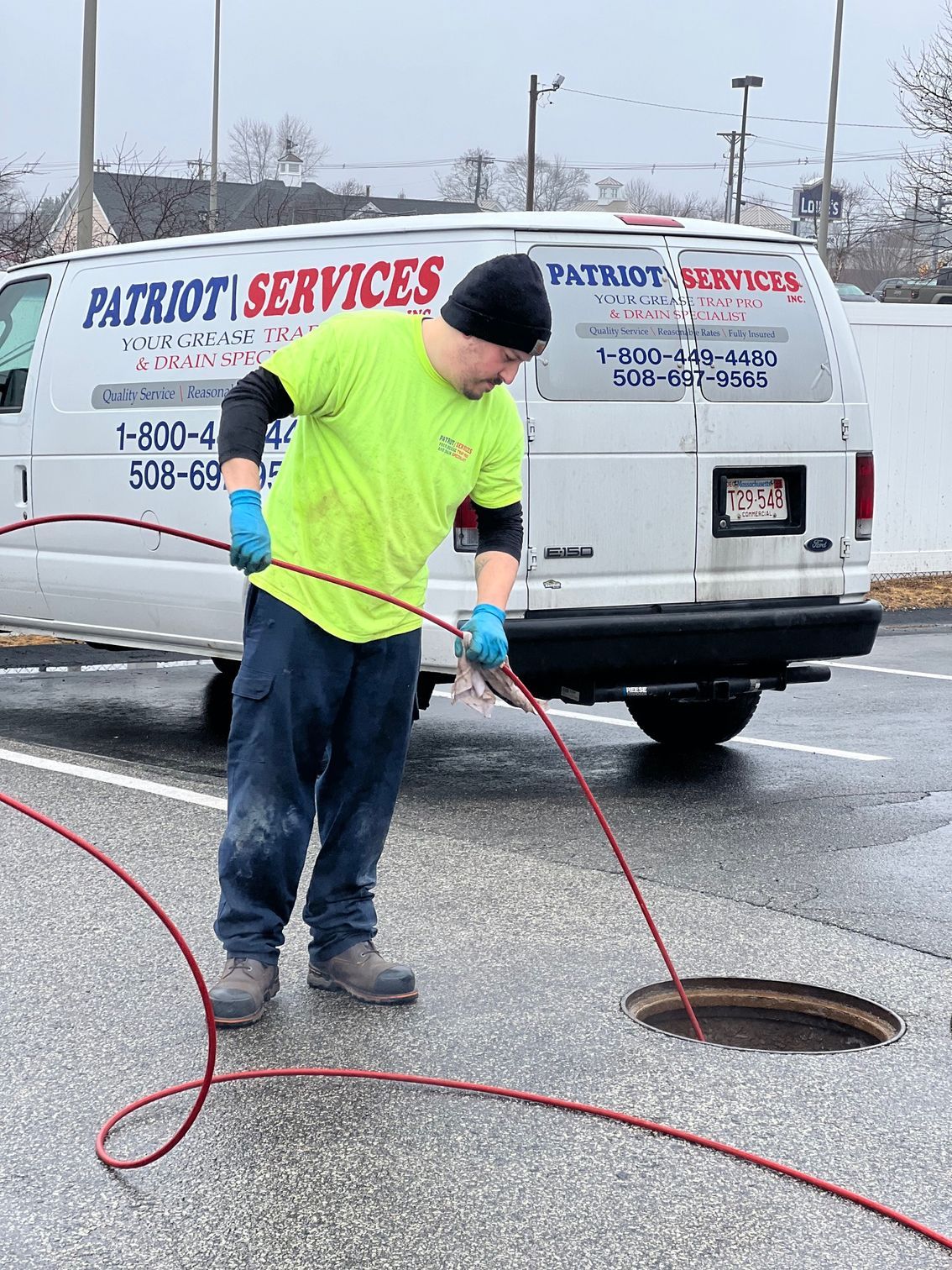 Man in neon green shirt working on a sewer, near a white van labeled Patriot Services.